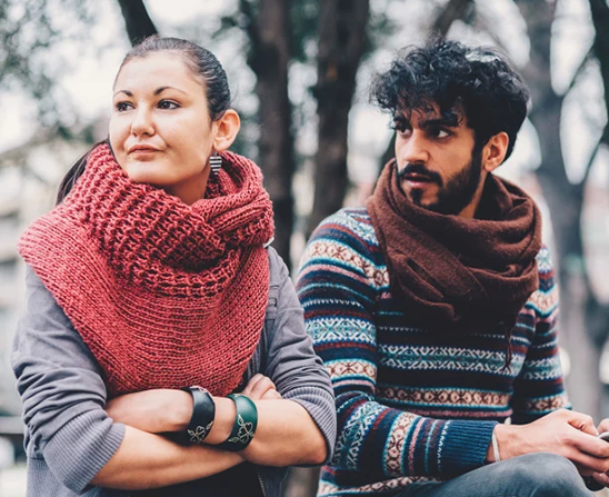 two people wearing sweaters sitting outside